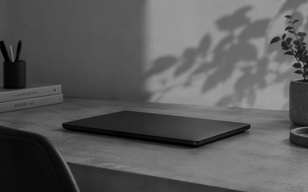 Closed laptop on a concrete desk beside books and a plant